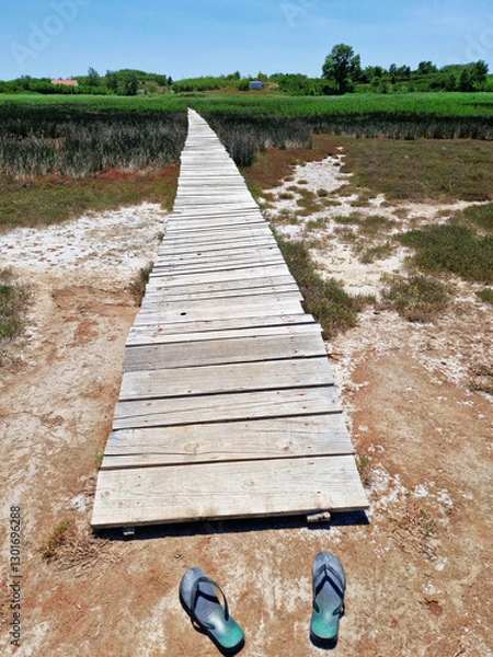 Obraz Wooden boardwalk through marshland with abandoned flip-flops in foreground