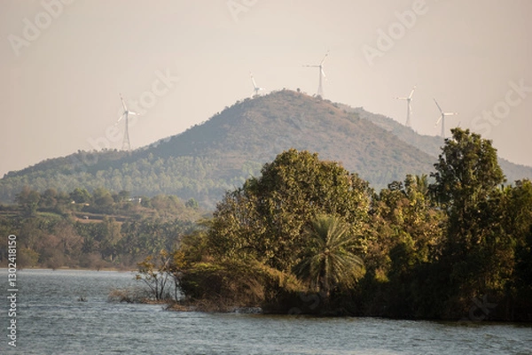 Fototapeta Wind turbines on a mountain overlooking a serene lake with lush greenery on a clear day