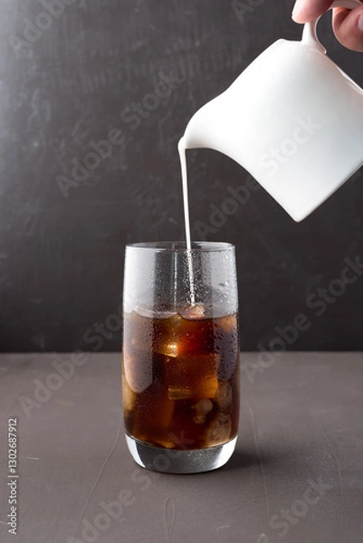 Obraz Milk pouring from a milk jug into a glass of iced coffee.