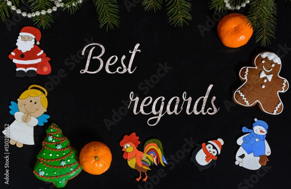 Fototapeta Xmas composition with text Best Regards on school blackboard and the Christmas decorations, toys (Santa Claus, Angel, a rooster, a snowman, a penguin) and tangerine