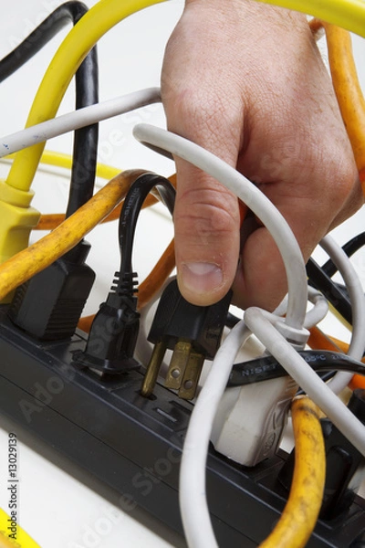 Fototapeta Plugging a cord into a tangled surge protector.