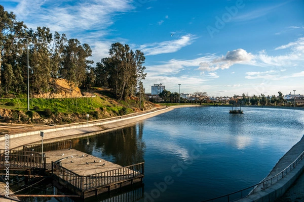 Fototapeta Lake of the park Moret with the blue sky and white clouds. The park is the biggest green space of the city of Huelva in Spain