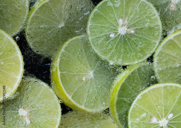 Fototapeta Close up of fresh lime slice in sparkling water with bubbles