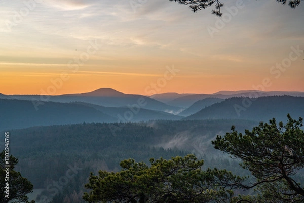 Fototapeta Sunrise on a rock with a summit cross and a view over a forest. Morning mood with fog in the middle of nature. Landscape in the Palatinate Forest, German
