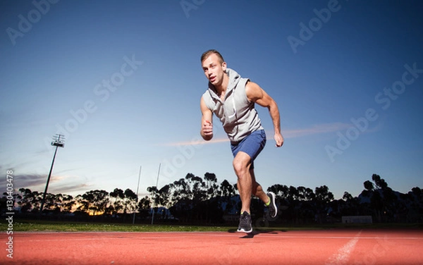 Fototapeta Male sprinter athlete on a tartan athletic track getting ready f