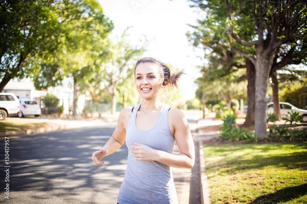 Fototapeta Female fitness model running and jumping in a street in a suburban area while training