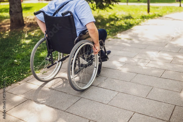 Fototapeta Close up image of man in wheelchair rolling on pathway in park.