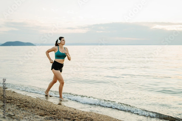 Fototapeta Young caucasian woman run or jog on the beach at sunset	