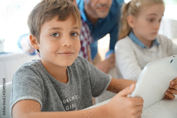 Fototapeta Portrait of schoolboy in classroom learning with digital tablet