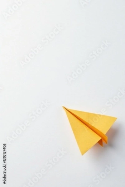 Fototapeta A solitary, handcrafted paper airplane, crafted from bright yellow paper, rests on a pristine white surface, poised for flight, symbolizing dreams of journey and exploration.