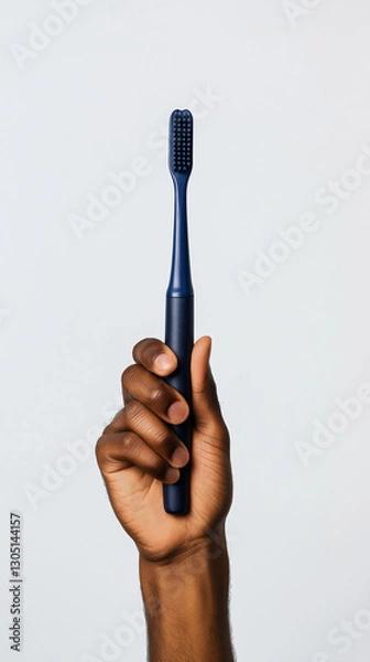 Obraz Dark-toned hand holding a dark blue toothbrush against a white background.