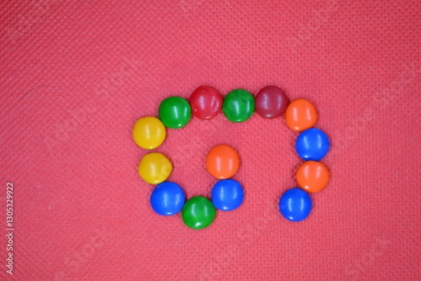 Fototapeta colored chocolate coated candy alphabet on pink background G