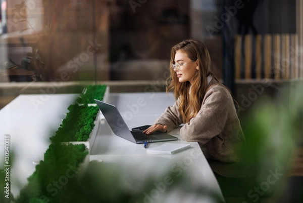 Fototapeta Business Woman working on a laptop in a modern office with greenery and coffee
