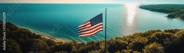 Obraz A stunning aerial view of the American flag waving in front of Lake Michigan, with lush green forests and blue waters stretching into the distance.