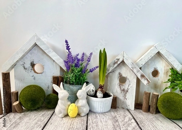 Obraz Easter decorative composition, home decoration for the holiday of bright Easter. On the table are cute rabbits and wooden houses, front view.
