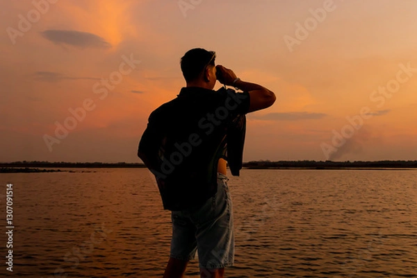 Fototapeta Man using binoculars to view the sunset.