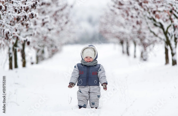 Obraz Little kid in snowsuit, hat and scarf, walking through a snowy path
