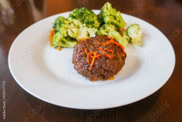Fototapeta meat cutlet with carrots and broccoli on a white plate on a wooden table