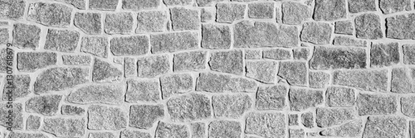 Fototapeta Black and white close-up of an irregular stone wall. The rough texture and natural patterns create a rustic and historical appearance. Ideal for backgrounds, textures. Long banner.