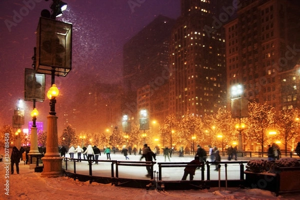 Fototapeta Winter night in Chicago. People enjoying ice skating at Millennium park ice rink during snowy night in Chicago.
