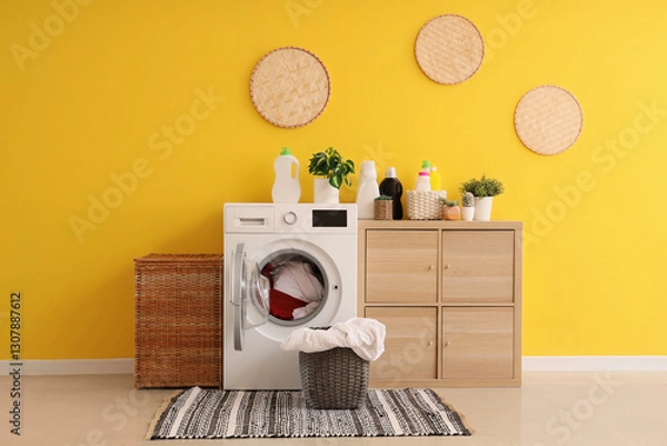 Fototapeta Modern washing machine, chest of drawers and laundry baskets near yellow wall in room