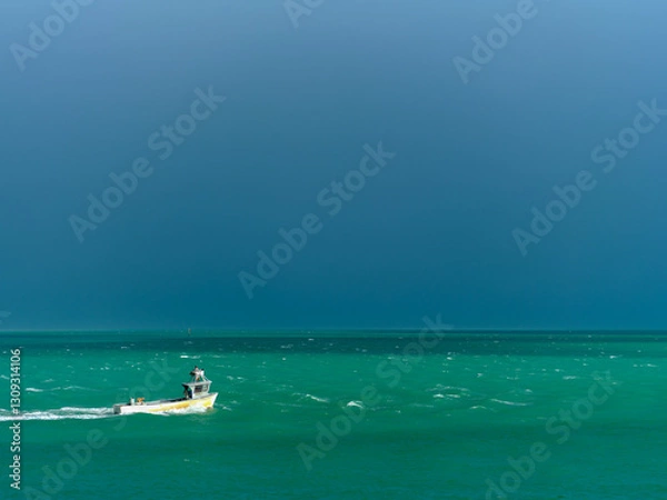 Fototapeta A long shrimp boat heads towards the harbor in the gulf ahead of the storm remnants of Hurricane Milton fighting through the white caps on the turquoise waters