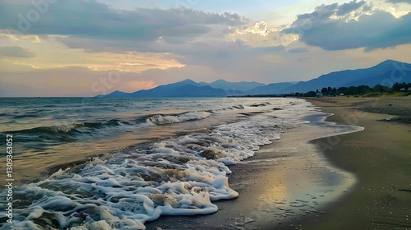 Obraz A scenic view of a beach at evening, with gentle sea waves, distant mountains, and a tranquil sunset sky.