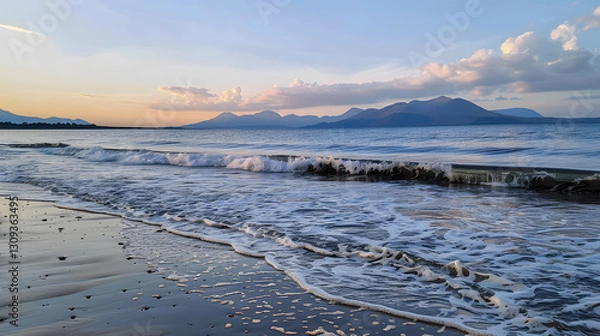 Obraz A scenic view of a beach at evening, with gentle sea waves, distant mountains, and a tranquil sunset sky.