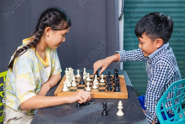 Fototapeta Smart kids enjoying a board game, making their next move in a friendly chess match.