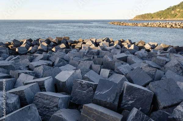 Fototapeta Rocks meet the sea. Breakwater texture. Coastal scene. Horizon line. Light and shadow play.