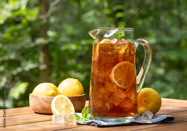 Fototapeta Pitcher of ice tea with lemon slices and mint outdoors on wooden table