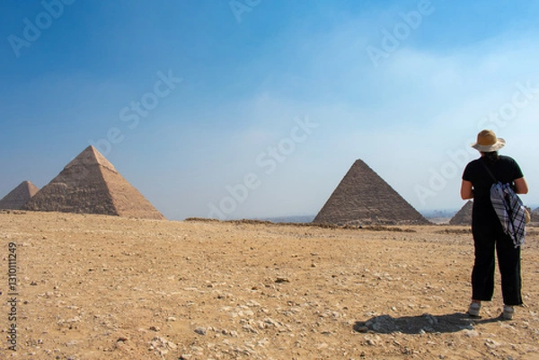 Fototapeta Young Woman looking at Giza Necropolis, Famed archaeological site featuring the Great Pyramids, the Great Sphinx and The Great Pyramid of Giza in the desert of Giza, Cairo, Egypt.