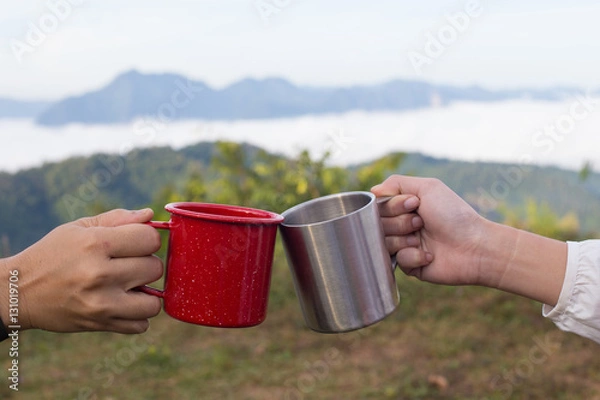 Fototapeta Cheers lass of two people make a toast at the mountain top view from their camping site with red and silver glass