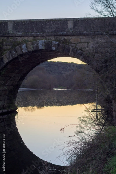 Fototapeta Roman bridge of Caparra Extremadura with a single eye and a vertical reflection in the water