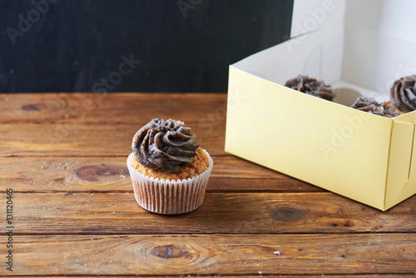 Fototapeta Single tasty chocolate cup cake with paper box over wooden background with a lot of space for the text.