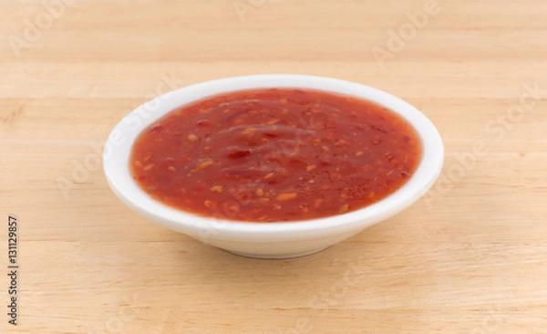 Fototapeta Chili chicken sauce portion in a small bowl atop a wood table.