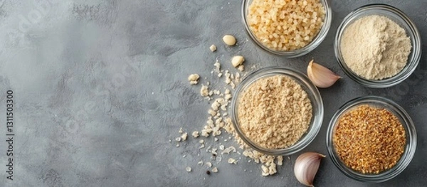 Fototapeta Dried garlic flakes granules and powder in clear glass bowls arranged on a grey textured surface with raw garlic cloves scattered around