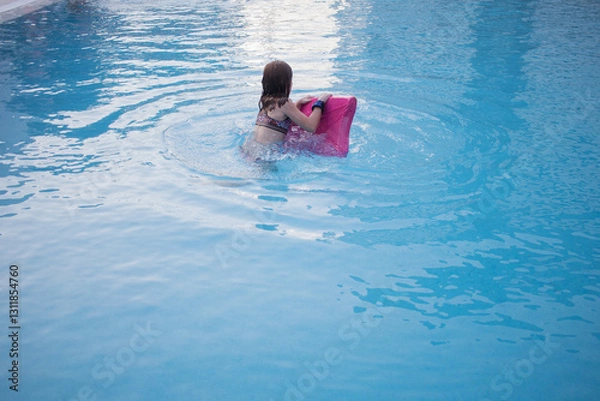 Obraz Red-haired girl playing with a pink surfboard in the pool. Water. Horizontal. Copy space. Blue
