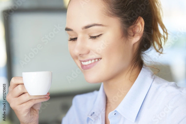 Fototapeta Coffee break in the office. Close-up shot of young assistant drinking a cup of coffee while sitting in the office.