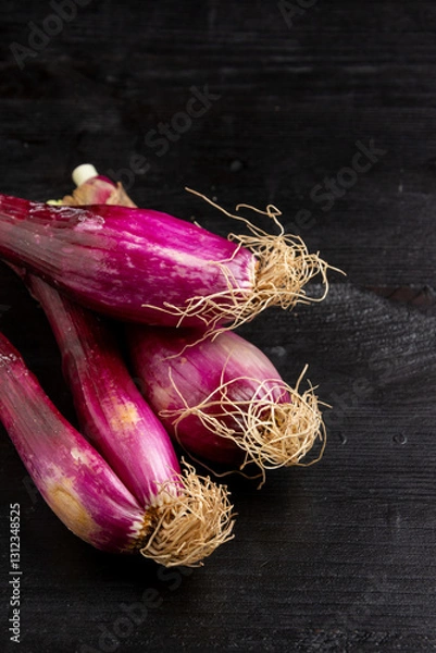 Fototapeta Top view of purple spring onions on dark wooden table, vertical with copy space