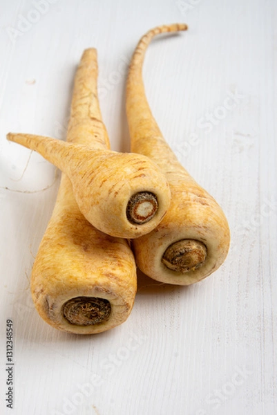 Fototapeta Top view of three parsnips on white wooden table, vertical with copy space