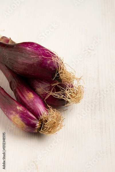 Fototapeta Top view of purple spring onions on white wooden table, vertical with copy space