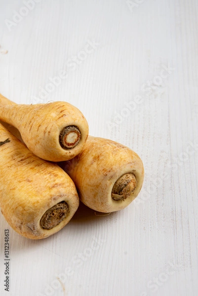 Fototapeta Aerial view of parsnips on white wooden table, vertical with copy space