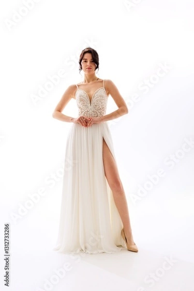 Fototapeta Elegant model showcasing a beautiful bridal gown with intricate detailing and a thigh-high slit in a pristine studio setting