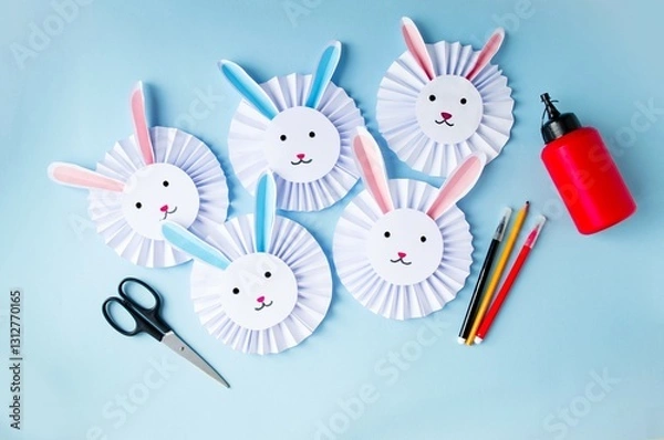 Obraz Paper craft on a blue background cute, funny Easter bunnies made of paper, glue, scissors, felt-tip pens.  Concept holiday Easter, spring children's creativity, handmade.  Flat lay, top view.