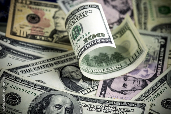 Obraz Half rolled hundred us dollar bill lying on different us dollar bills. Background. Selective focus.