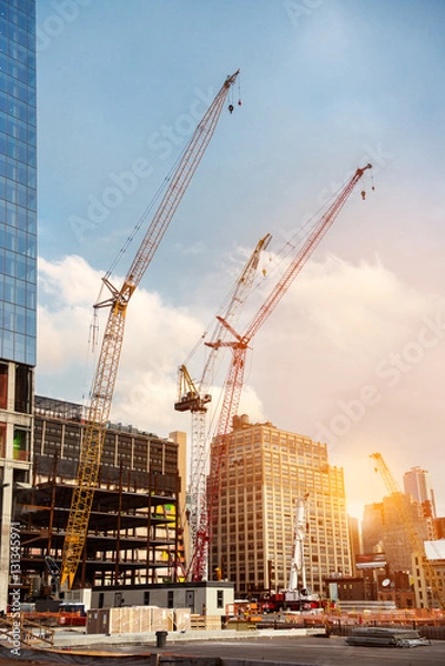 Fototapeta Construction cranes on construction site build office skyscraper building in New York City at sunset time.