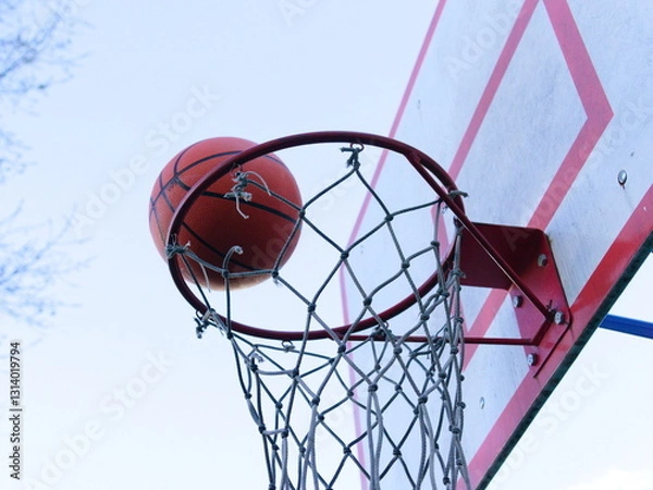Fototapeta A basketball is flying into a basket on the street. Playing basketball and sports
