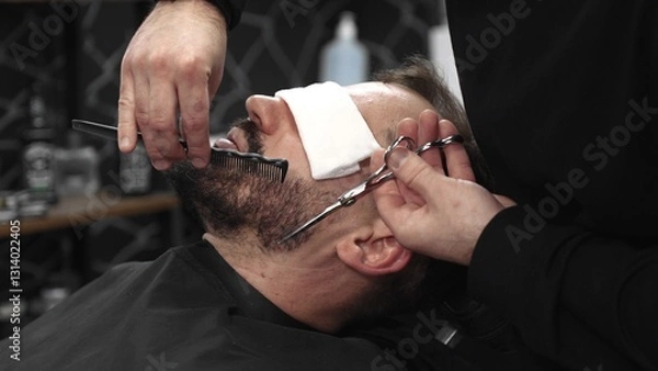 Fototapeta Professional barber carefully trimming beard with scissors, creating clean lines and sharp detailing inside contemporary barbershop workspace