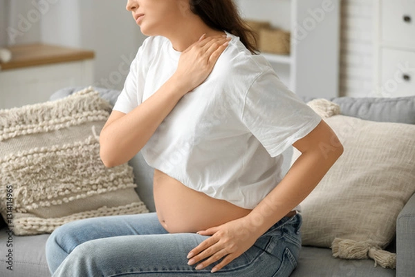 Fototapeta Young pregnant woman suffering from shoulder pain on sofa at home, closeup